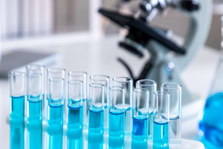 Test tubes with blue liquid in holder with microscope in background. Science glass equipment in...