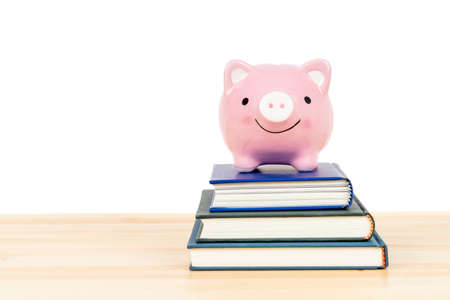 Pink piggy bank on top of books on wooden desk on white background, concept saving for education and scholarshipの写真素材