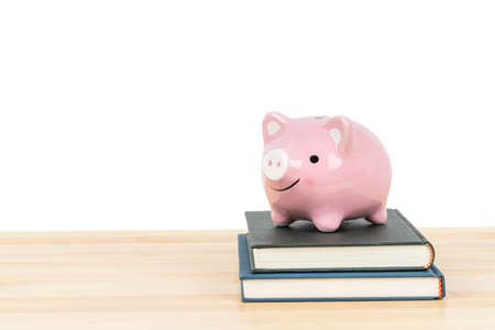 Pink piggy bank on top of books on wooden desk on white background, concept saving for education and scholarshipの写真素材
