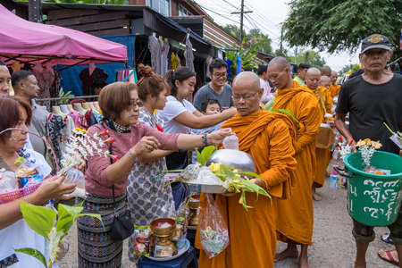 Kanchanaburi, Thailand - October 15, 2019: Buddhist monk in orange yellow robe waking in line and...