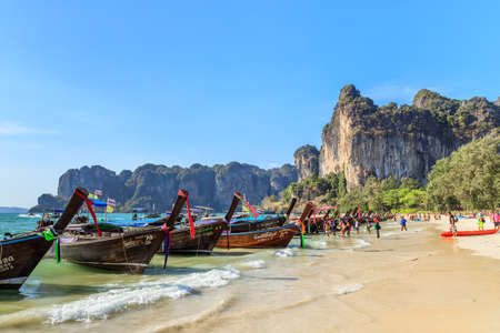 Krabi, Thailand - February 16, 2020: Long tail boat and turquoise crystal clear sea water with limestone cliff and mountain at Railay Beach.のeditorial素材