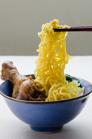 Chopsticks Hold Egg Noodle Stewed Chicken Drumstick from Bowl.の写真素材