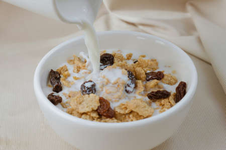 Pouring Milk in Bowl of Cereal and Raisin for Breakfast Meal.の写真素材