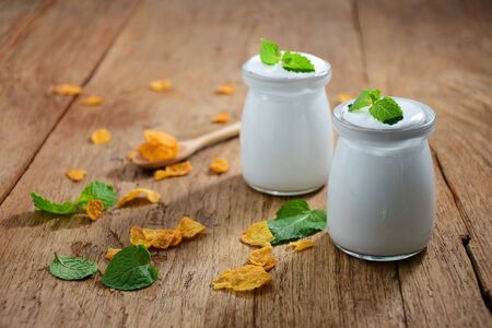 Breakfast yogurt in a glass jar with a spoon on an old wooden floorの写真素材