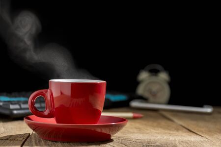 The red coffee cup is placed on the desk. The old wood has a computer and the phone is also placed.の写真素材
