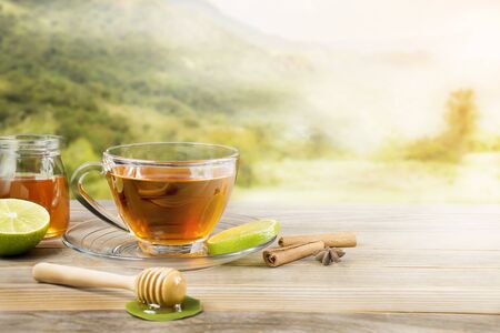 Tea cup with honey and lemon placed on a wooden table, natural background, warm morning atmosphereの写真素材