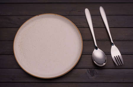 Empty white ceramic plates with spoons and forks arranged on an old black wooden table - top view.
