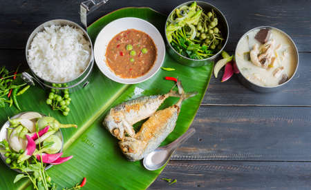 Fried mackerel with shrimp paste sauce with jasmine rice and chicken tom kha set. Thai food on a black wooden tableの写真素材