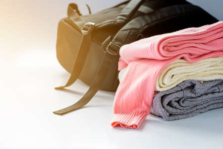pink, white and gray sweater folded over a white background with a black backpack. And a soft...