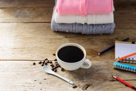 White coffee cup With black coffee and a pink white gray knit sweater and a pencil book on an old...