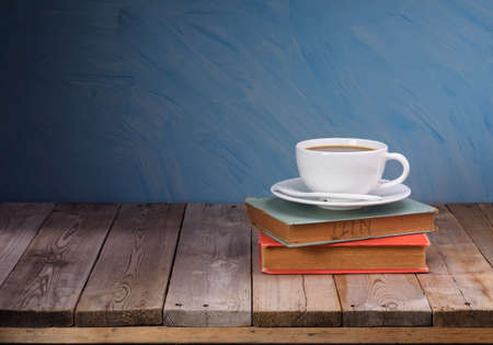 White coffee cups and dark black coffee are placed on a pile of old books on an old wooden table....