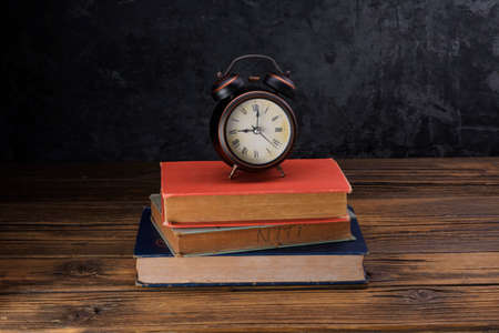Alarm clock placed on old books on old wooden table black wall background