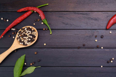 Red chili and peppers in a wooden spoon placed on a dark vintage wooden table top view