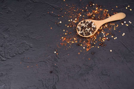 Pepper in a wooden spoon And cayenne pepper scattered on a black table top viewの写真素材