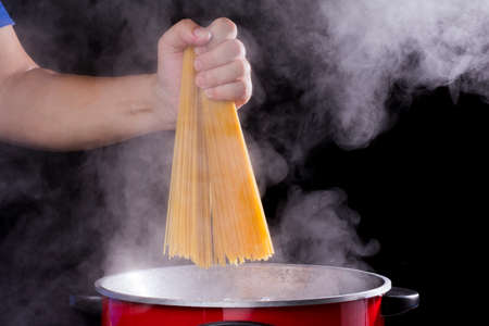 the chef put spaghetti in the pot or a pan of boiling water with hot steam or smoke on a dark black backgroundの写真素材