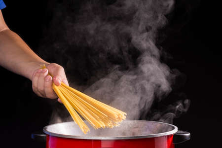 the chef put spaghetti in the pot or a pan of boiling water with hot steam or smoke on a dark black backgroundの写真素材