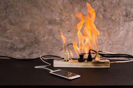 Short circuit An electrical outlet or electronic device bursts into flames while charging a mobile phone battery. Using a substandard plug or cordの写真素材