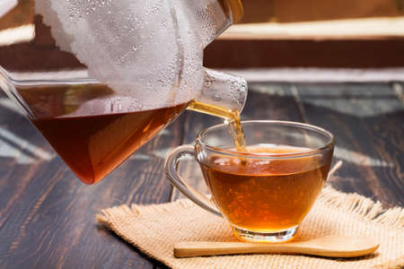 Close-up shot of hot tea or coffee poured into a cup placed on the desk. or a table to sit and drink coffee at work or at home near the window at sunset or in the morningの写真素材