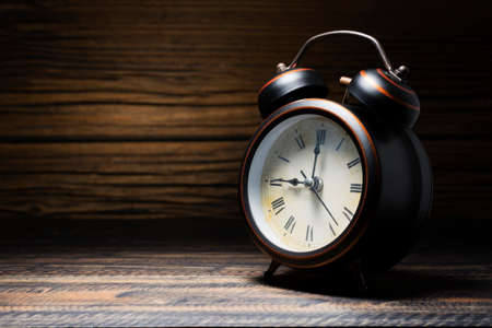retro style black alarm clock placed on a dark wooden table on a black backgroundの写真素材