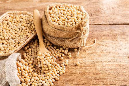 soybean seeds in a wooden spoon and in a sack set on a wooden table Seeds or natural healthy food -...