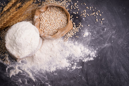 Flour and wheat grains in sacks with wheat ears On a black background table. In a rustic kitchen. Top view.の写真素材