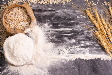 Flour and wheat grains in sacks with wheat ears On a black background table. In a rustic kitchen. Top view.の写真素材