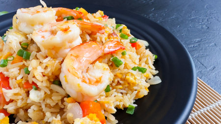 close up-Fried rice with vegetables and sea prawns, carrots, eggs, and tomatoes. Thai Chinese food is arranged on a black plate on a black background kitchen table, top view.の写真素材