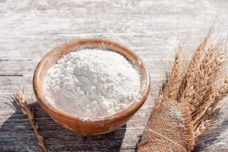 Soft focus, flour in a wooden bowl, ears of wheat, barley, cooking, bread, and cookies arranged on a wooden tabletop in a rustic kitchen, top view.の写真素材