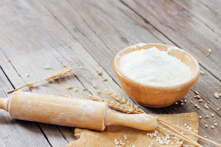 Soft focus, flour in a wooden bowl, ears of wheat, barley, cooking, bread, and cookies arranged on a wooden tabletop in a rustic kitchen, top view.の写真素材