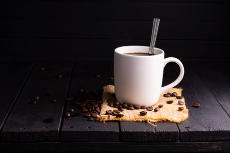 Freshly brewed coffee. Coffee cup or mug arranged on a black wooden table with roasted coffee beans. Espresso mocha cappuccino barista on dark background.の写真素材