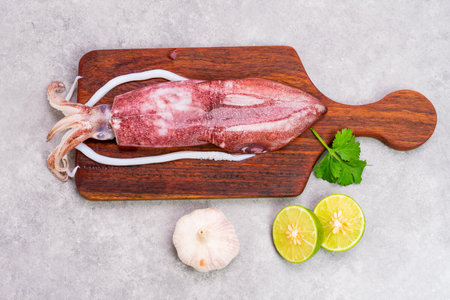 Fresh raw octopus on wooden chopping board background Seafood squid with lemon top view and copy...