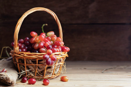 Red grapes, naturally sweet fruit, are placed on a wooden table and arranged in a wooden basket. on the old wooden backgroundの写真素材