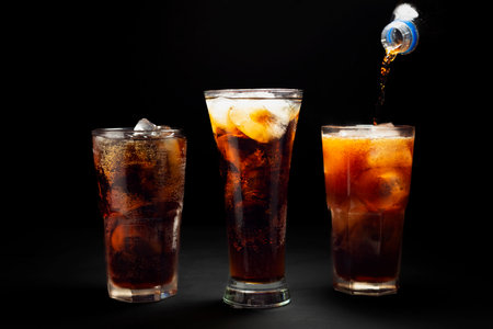 Black soda. Close-up of pouring soda with ice in a glass. Placed on a black and dark background.の写真素材