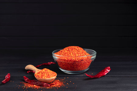 Chili powder, dried chilies, spicy condiments in a bowl placed on a table, dark background.の写真素材