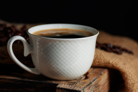 Close-up of hot coffee in a coffee cup With roasted coffee beans arranged on a table on a black and dark background.の写真素材