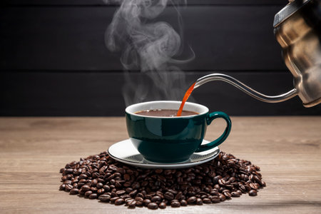Pouring hot coffee into a green coffee cup With roasted coffee beans on a wooden table, dark black background.の写真素材