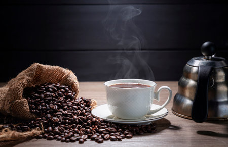 Hot coffee in a white coffee cup With roasted coffee beans on a wooden table, dark black background.の写真素材