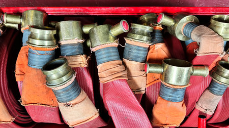 Red fire hose with gold or brass nozzles rolled up and stored in a container, ready for use by...