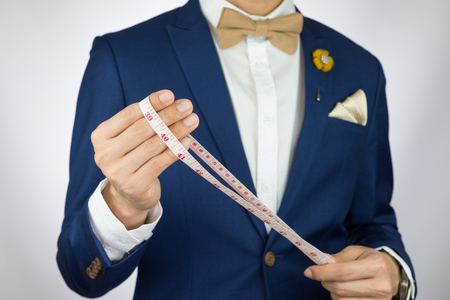Man in blue suit with coffee cream bowtie color, flower brooch, and dot pattern pocket square carry measurement tapeの写真素材