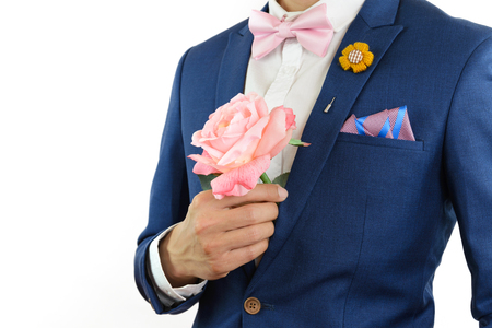 Man in blue suit with pink bow tie, flower brooch, and pink blue strip pocket square, close up, carry flowersの写真素材