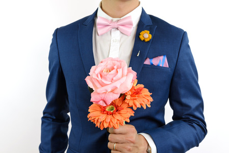 Man in blue suit with pink bow tie, flower brooch, and pink blue strip pocket square, close up,...