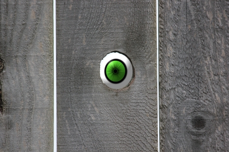 Green eyeball looking in through an open knot hole in a weathered wooden fence leaving room on the fence for your saying の写真素材