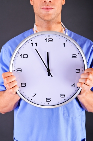 Surgeon with wall clock over dark backgroundの写真素材