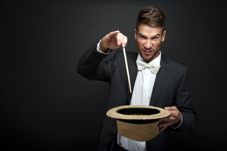 A magician in a black suit holding an empty top hat and magic wand の写真素材
