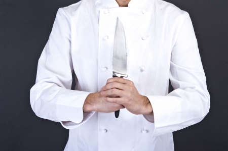 Portrait of a young cook man wearing uniform holding a knife over grunge background.の写真素材