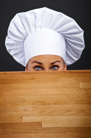 chef woman on dark background in shock behind wooden boardの写真素材