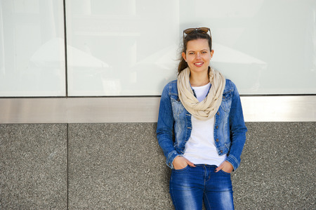 Beautiful urban woman, girl standing by the wall in city wering jeans jacketの写真素材