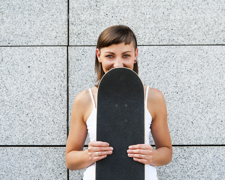 Young girl with skateboard near her face in city by the wall.の写真素材