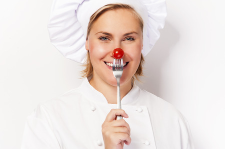 Chef woman holdinh a fork with tomato against her nose, standing against white background smiling.の写真素材