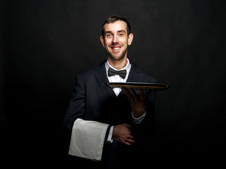 Waiter in black suit holding tray over black background.の写真素材